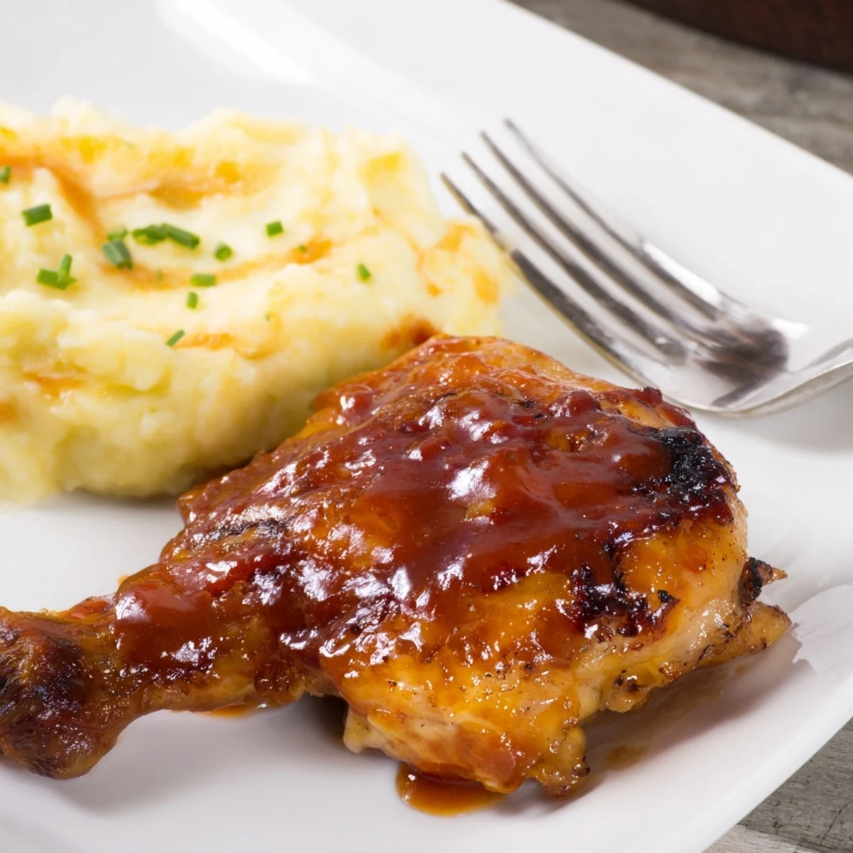 Succulent honey BBQ chicken thighs served with creamy garlic mashed potatoes on a plate.  