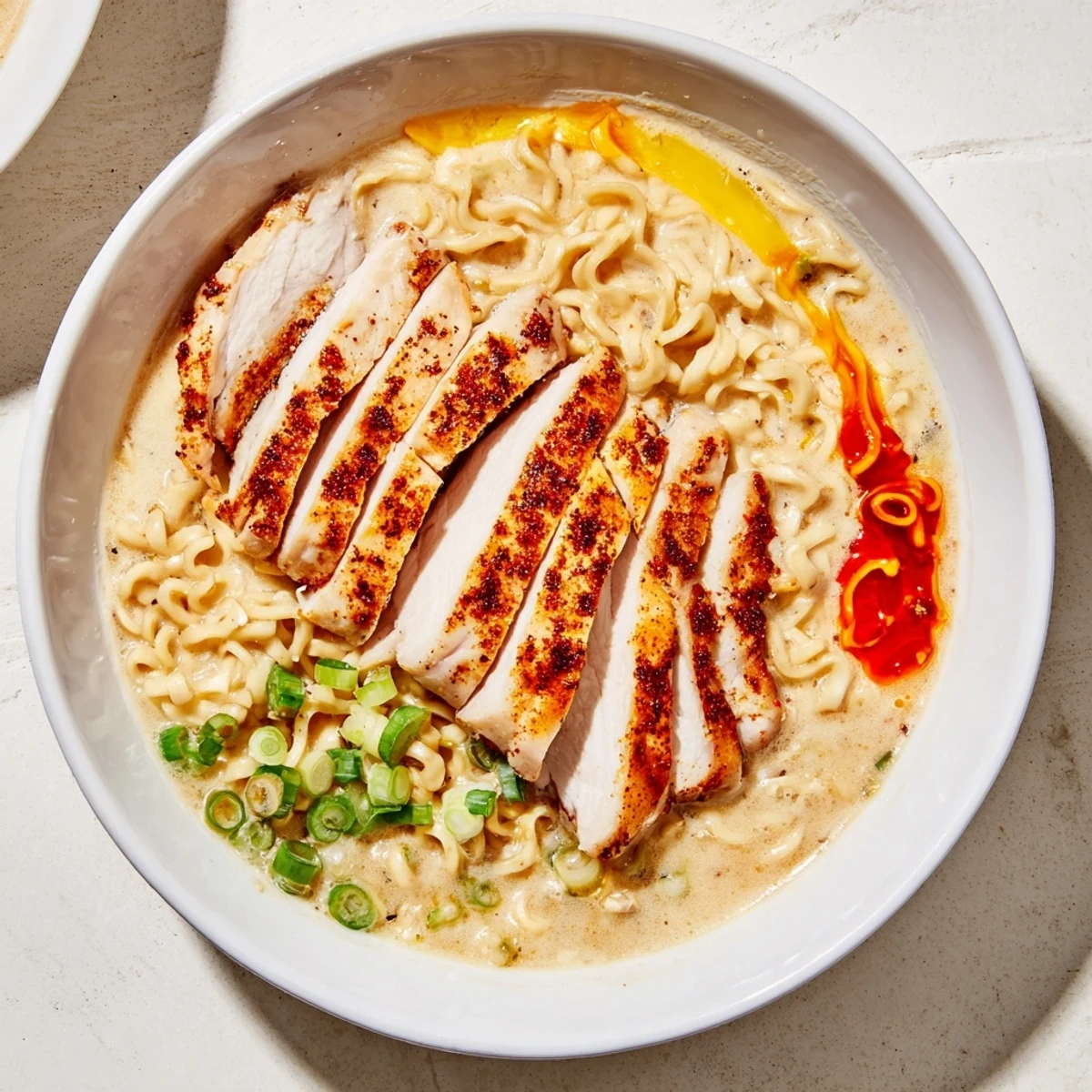 Close-up of Fiery Chicken Ramen: Tender chicken, creamy sauce, garnished with green onion, ready to be enjoyed.