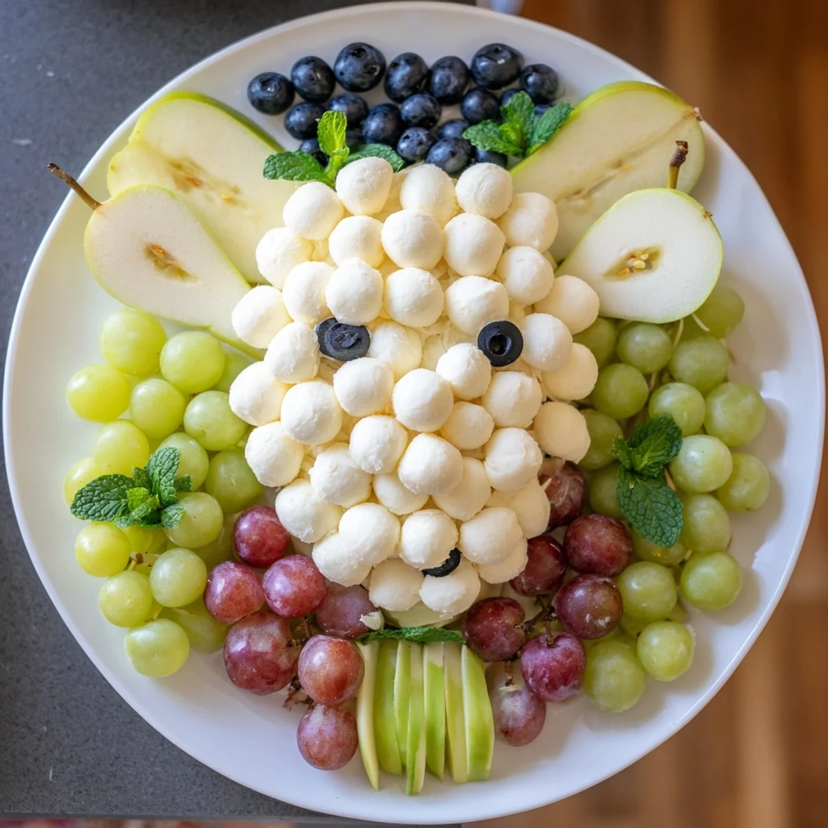Vibrant lamb face fruit and cheese platter featuring juicy grapes and olives as facial features.