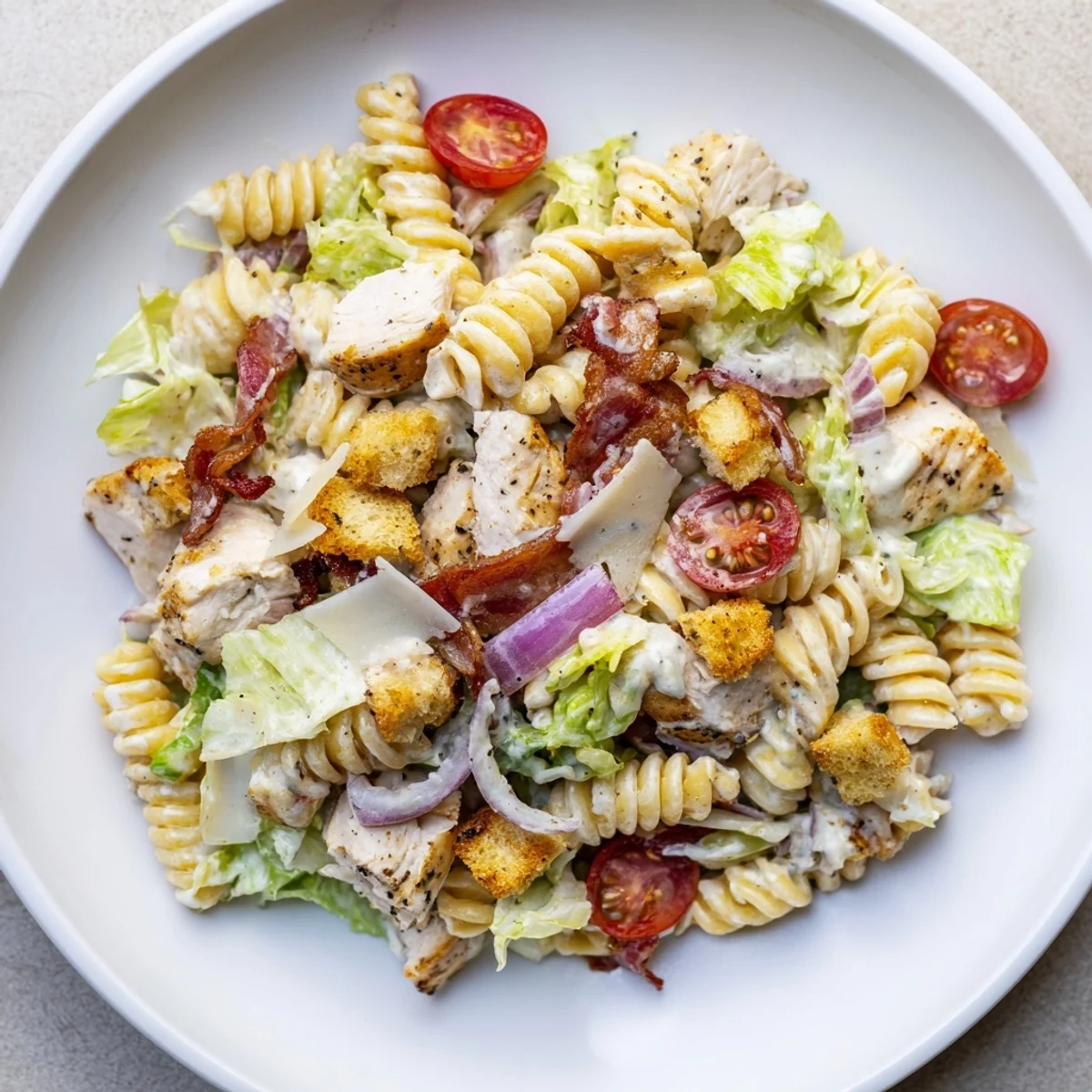 Close-up of a bowl of Chicken Caesar Pasta Salad: rotini with grilled chicken and crunchy bacon.