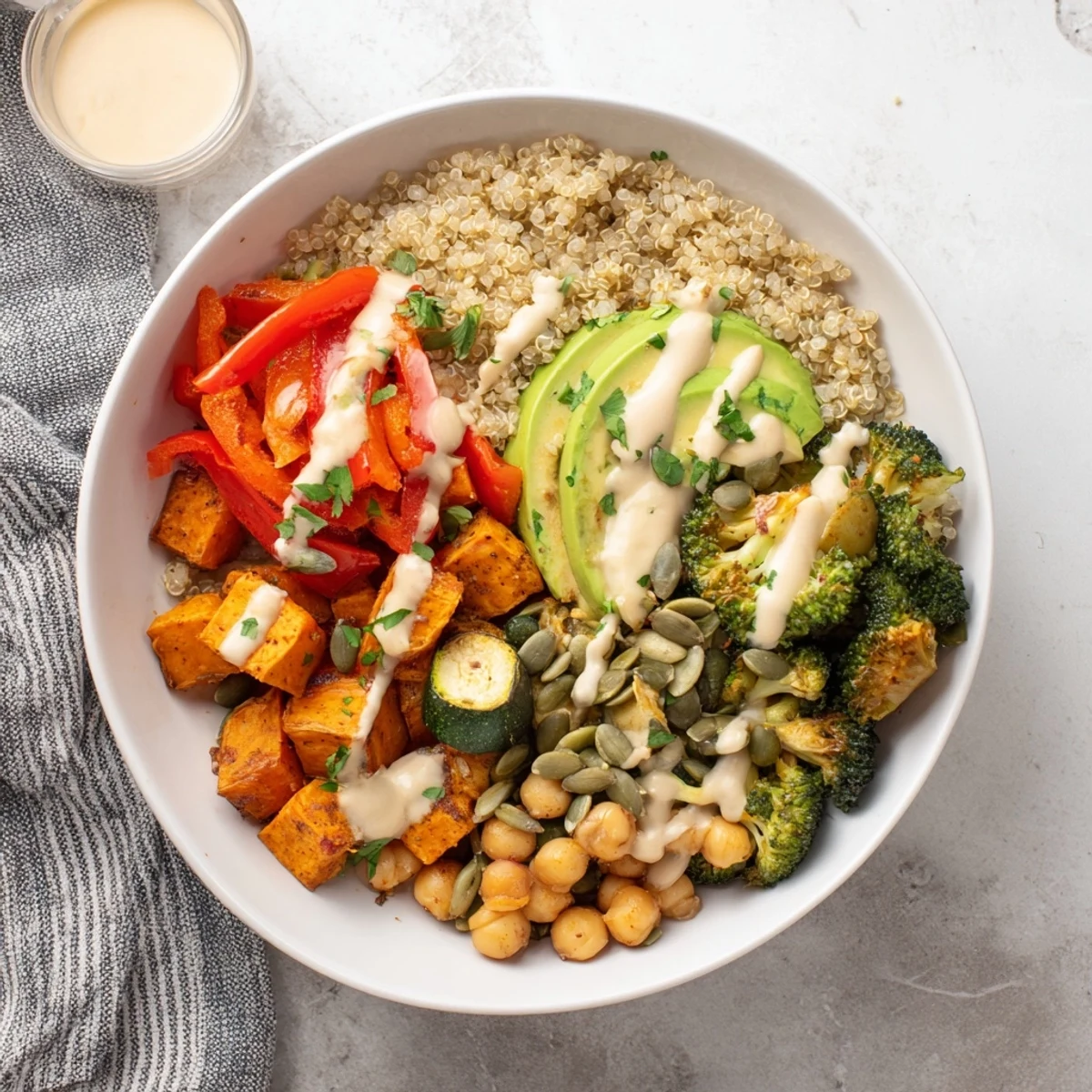 Healthy vegan quinoa Buddha bowl topped with roasted broccoli, bell pepper, zucchini, and avocado slices.