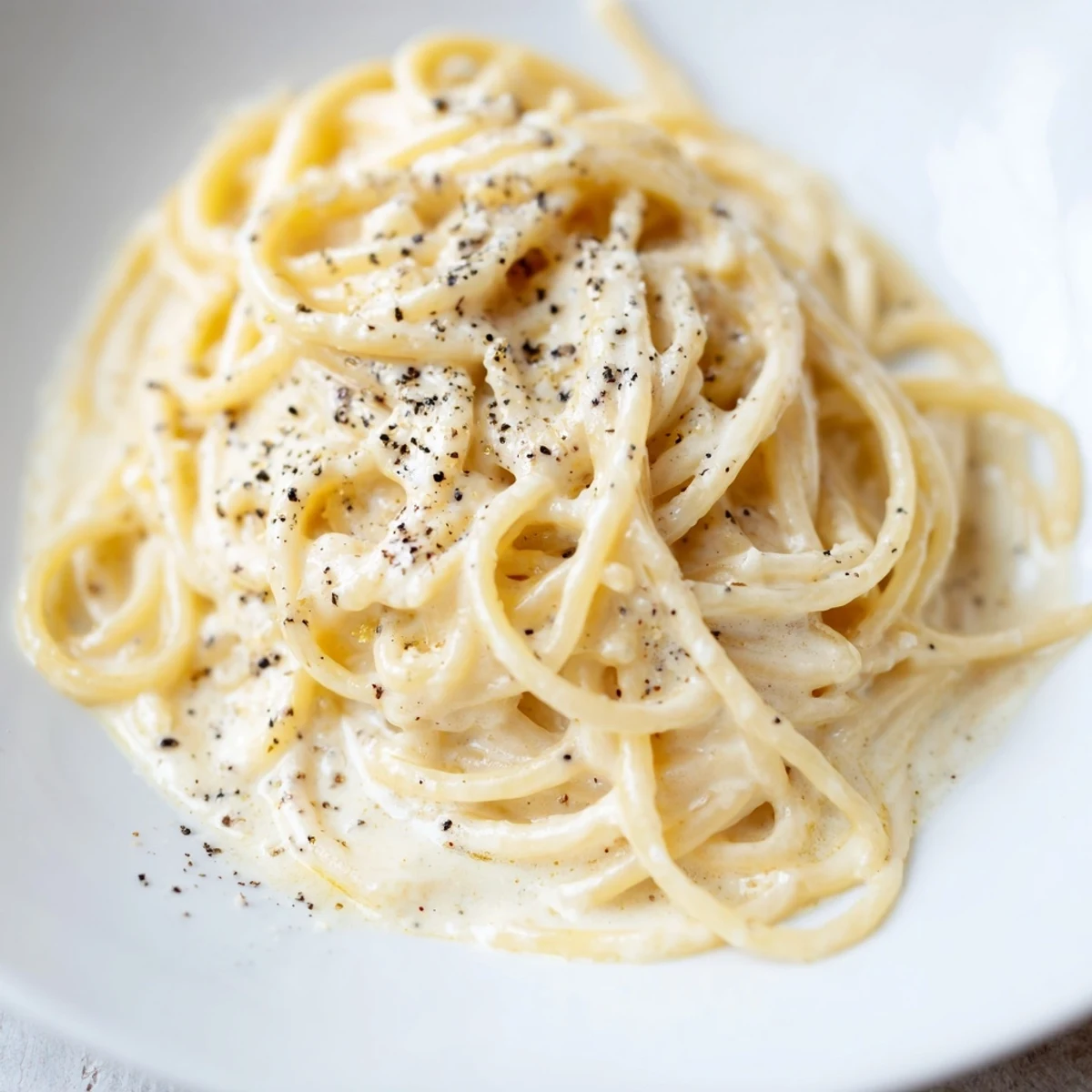 Steaming plate of Spaghetti Cacio e Pepe garnished with extra cheese, served alongside a glass of crisp Pinot Grigio.  