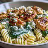 A close-up of Greek Chicken Feta Pasta Skillet showing rich yogurt sauce, fusilli pasta, and fresh parsley garnish with lemon wedges.