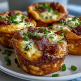 Twelve savory Ranch & Cheddar Egg Muffin Cups are arranged on a white plate, garnished with green chives for a fresh pop.