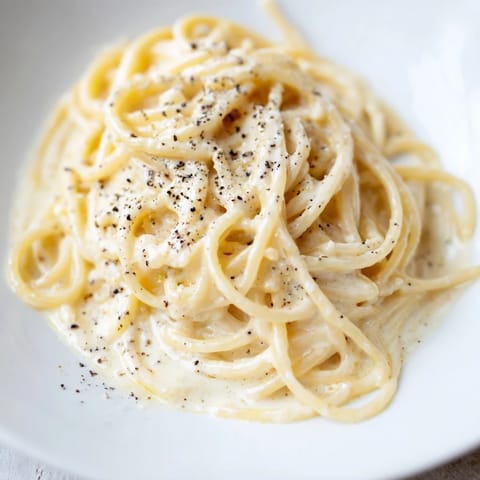 Steaming plate of Spaghetti Cacio e Pepe garnished with extra cheese, served alongside a glass of crisp Pinot Grigio.  