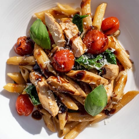 A close-up of Balsamic Glazed Chicken Pasta topped with grated Parmesan and fresh basil leaves on a rustic plate.  