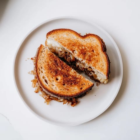 A close-up view of a Caramelized Onion & Gruyère Grilled Cheese, featuring crispy country bread crust and rich, nutty Gruyère oozing out.  