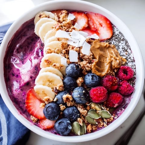 Thick purple acai berry smoothie bowl garnished with fresh strawberries, coconut flakes, pumpkin seeds, and a drizzle of almond butter for extra protein.