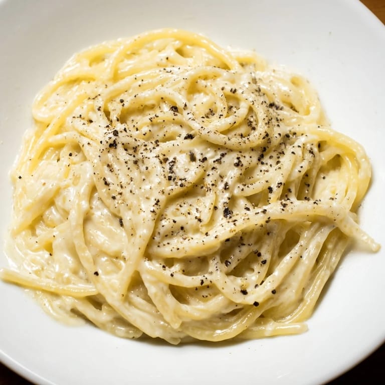 Fork lifting a portion of Spaghetti Cacio e Pepe, showing the creamy, emulsified sauce clinging to each strand.