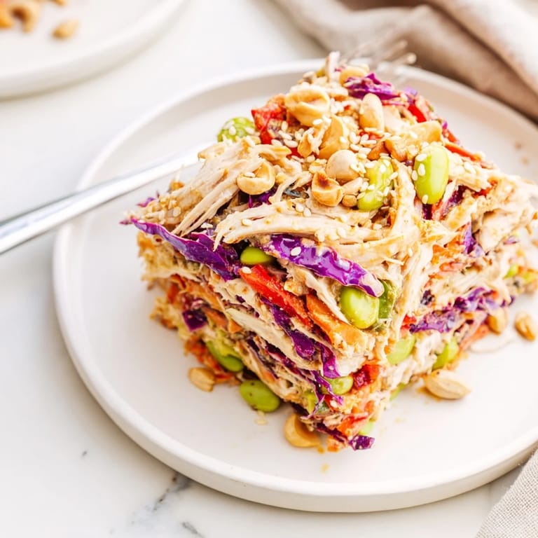 A close-up of the Asian-inspired Edamame Crunch Chicken Salad, garnished with toasted sesame seeds and optional crunchy cashews on a rustic wooden table.