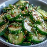 Asian Cucumber Salad with Sesame and Rice Vinegar: crisp cucumbers in tangy sesame dressing, garnished with green onions and sesame seeds.